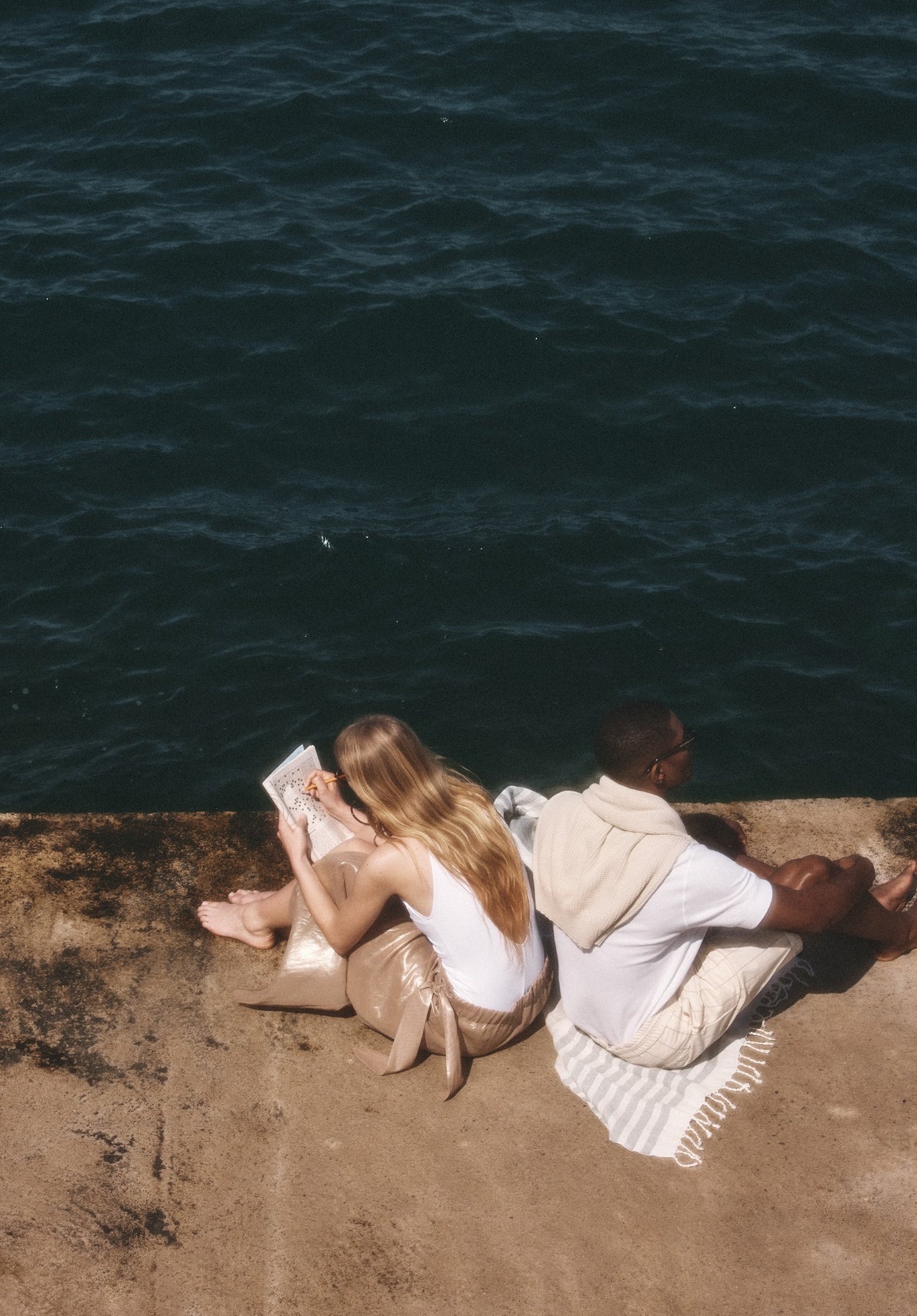 A man and women sitting on river shore reading book